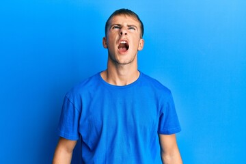 Young caucasian man wearing casual blue t shirt angry and mad screaming frustrated and furious, shouting with anger. rage and aggressive concept.
