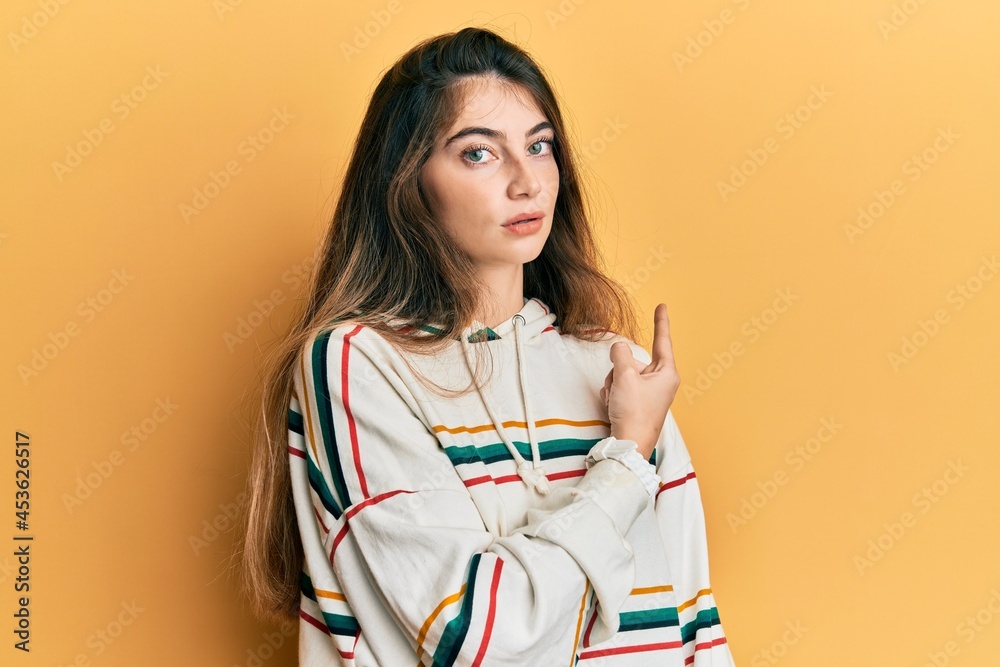 Poster Young caucasian woman wearing casual clothes pointing with hand finger to the side showing advertisement, serious and calm face