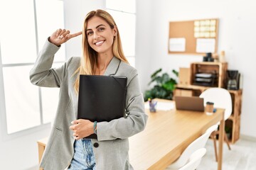 Blonde business woman at the office smiling pointing to head with one finger, great idea or thought, good memory