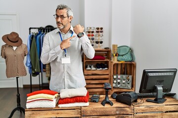 Middle age hispanic man working as manager at retail boutique in hurry pointing to watch time,...