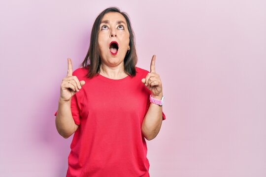 Middle age hispanic woman wearing casual clothes amazed and surprised looking up and pointing with fingers and raised arms.