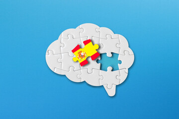Spanish learning concept, white jigsaw puzzle pieces with spanish flag a human brain shape on blue background	
