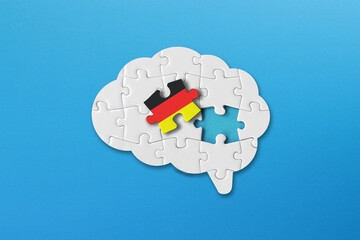 German learning concept, white jigsaw puzzle pieces with germany flag a human brain shape on blue...