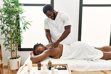 Obraz na płótnie Canvas Young physiotherapist man smiling happy giving back massage to african american woman at the clinic.