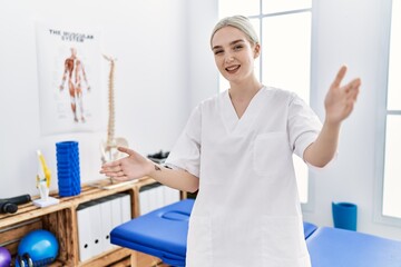 Young caucasian woman working at pain recovery clinic looking at the camera smiling with open arms for hug. cheerful expression embracing happiness.