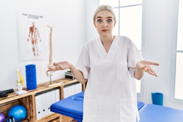 Young caucasian woman working at pain recovery clinic clueless and confused with open arms, no idea concept.