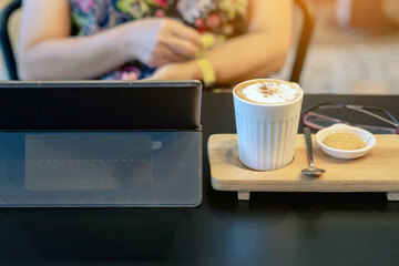 Hot Cappuccino coffee for quarantined woman wear face mask and work from home by using tablet and stress relief with hot coffee. Concepts of Covid-19 (Coronavirus disease). Selective focus on coffee.