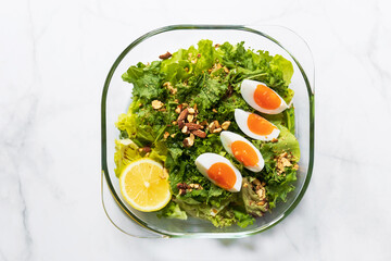 Green salad and kale with boiled egg, almond, nuts and lemon on white marble table; top view and copy space.