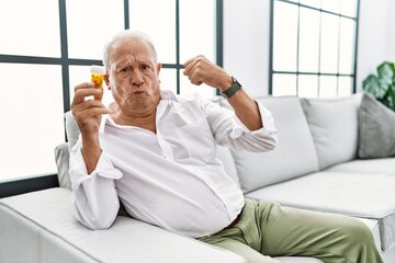 Senior man holding pills strong person showing arm muscle, confident and proud of power