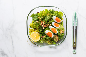 Green salad and kale with boiled egg, almond, nuts and lemon on white marble table; top view and copy space.