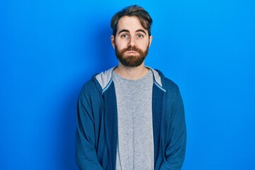 Caucasian man with beard wearing casual sweatshirt puffing cheeks with funny face. mouth inflated with air, crazy expression.