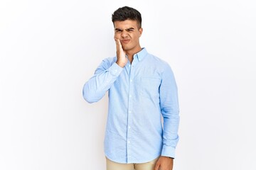 Young hispanic man wearing business shirt standing over isolated background touching mouth with hand with painful expression because of toothache or dental illness on teeth. dentist