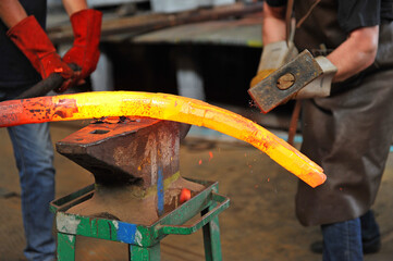 Blacksmiths manually forging the molten metal on the anvil.