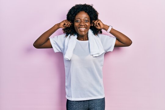 Young african american woman wearing sportswear and towel smiling pulling ears with fingers, funny gesture. audition problem