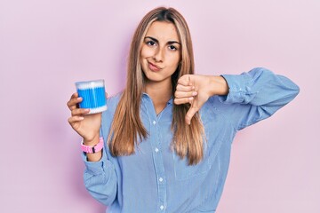 Beautiful hispanic woman holding earwax cotton removers with angry face, negative sign showing...