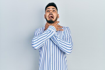 Young hispanic man with beard wearing casual striped shirt shouting and suffocate because painful strangle. health problem. asphyxiate and suicide concept.