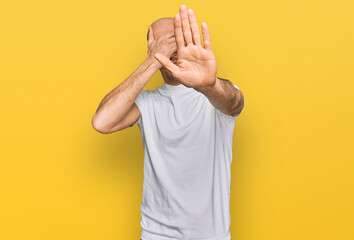 Plakat Bald man with beard wearing casual white t shirt covering eyes with hands and doing stop gesture with sad and fear expression. embarrassed and negative concept.
