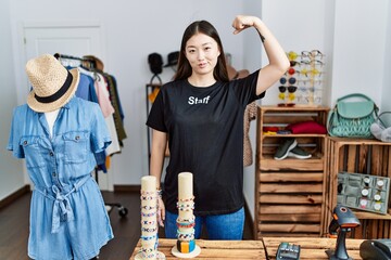 Young asian woman working as manager at retail boutique strong person showing arm muscle, confident and proud of power