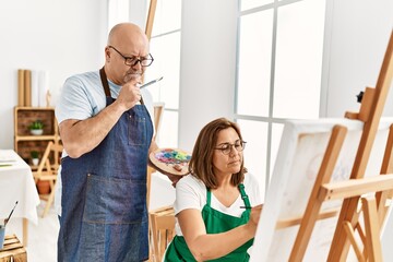 Middle age hispanic painter couple with serious expression painting at art studio.
