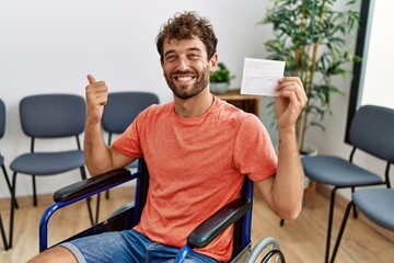 Young handsome man holding covid record card sitting on wheelchair pointing thumb up to the side...