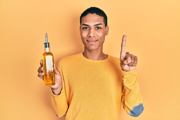 Young african american guy holding olive oil can smiling with an idea or question pointing finger...