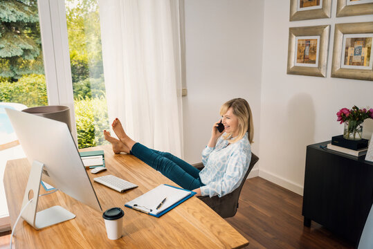 Attractive middle aged woman sitting at desk while having a call and working from home
