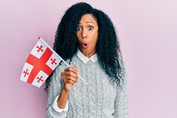 Middle age african american woman holding georgia flag scared and amazed with open mouth for surprise, disbelief face
