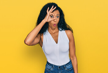 Middle age african american woman wearing casual style with sleeveless shirt doing ok gesture shocked with surprised face, eye looking through fingers. unbelieving expression.