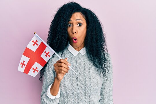 Middle Age African American Woman Holding Georgia Flag Scared And Amazed With Open Mouth For Surprise, Disbelief Face