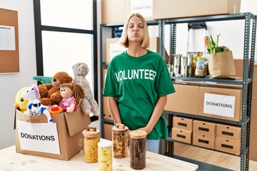 Young caucasian woman wearing volunteer t shirt at donations stand puffing cheeks with funny face....