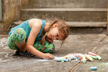 Little young school age child drawing with chalk on the concrete sitting on the ground. Art...