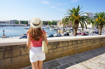 Rear view of young woman looking at harbour and cityscape of Bari, Italy