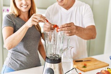 Middle age hispanic couple smiling happy cooking smoothie at the kitchen.