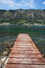 Long wooden pier against the backdrop of the beautiful Bay of Kotor, Montenegro. Very beautiful promenade and beach with clear blue water.