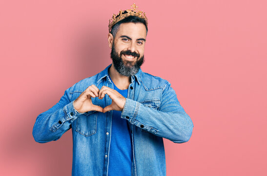 Hispanic man with beard wearing king crown smiling in love showing heart symbol and shape with hands. romantic concept.