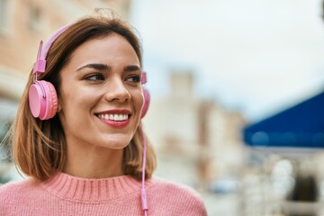 Young caucasian girl smiling happy using headphones at the city.