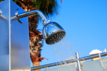 Closeup of outdoor shower head. Outdoor pool shower. Water running from poolside shower sprinkler