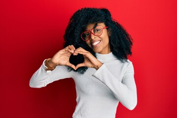 African american woman with afro hair wearing casual sweater and glasses smiling in love doing heart symbol shape with hands. romantic concept.