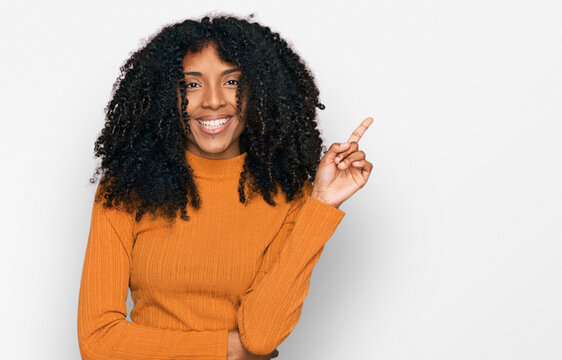 Young african american girl wearing casual clothes with a big smile on face, pointing with hand and finger to the side looking at the camera.