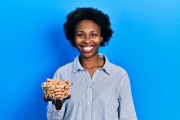 Young african american woman holding peanuts looking positive and happy standing and smiling with a confident smile showing teeth