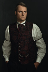 Shadowy portrait of a young man in vintage Victorian attire in front of a dark gray wall.
