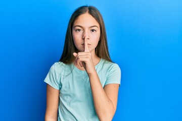 Beautiful brunette little girl wearing casual white t shirt asking to be quiet with finger on lips. silence and secret concept.