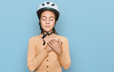 Beautiful brunette little girl wearing bike helmet smiling with hands on chest with closed eyes and grateful gesture on face. health concept.