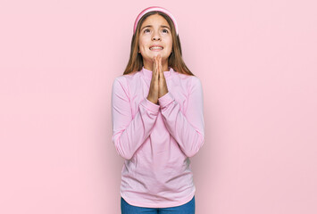 Beautiful brunette little girl wearing casual turtleneck sweater begging and praying with hands together with hope expression on face very emotional and worried. begging.