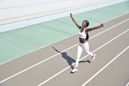 Top View Of Happy Young African Woman In Sports Clothing Running On Track And Keeping Arms Raised