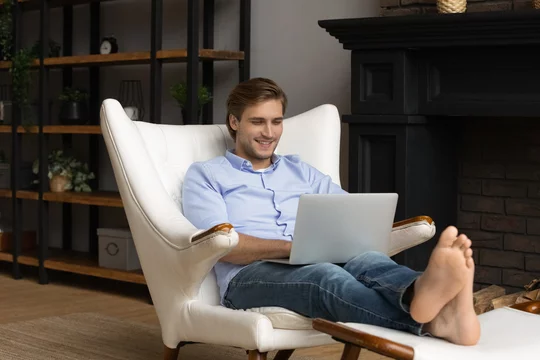 Happy millennial relaxed handsome man using computer resting in comfortable  armchair, putting feet on ottoman. Addicted to modern technology young guy  shopping in internet store or chatting online. Stock Photo | Adobe Stock