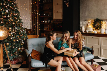 A group of happy cheerful women girlfriends celebrate Christmas holiday laugh congratulate give gifts sitting on the couch at a party at home in the loft style, selective focus