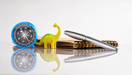 Compass, fountain pen and notepad next to a funny toy dinosaur - diplodocus. White reflective...