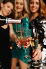 Funny girls friends in Santa hats celebrate the Christmas holiday laugh rejoice hold glasses drink champagne burn sparklers at a party in the decorated kitchen in the loft style of the house
