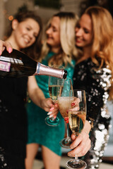 Funny girls friends in Santa hats celebrate the Christmas holiday laugh rejoice hold glasses drink champagne burn sparklers at a party in the decorated kitchen in the loft style of the house